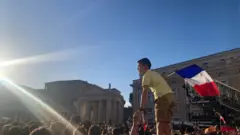 A young boy, dressed in a yellow shirt, and khaki shorts stand on his father's shoulder. After the announcement of the new Pope, he waved the French flag on St. Peter's Square.