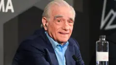 Martin Scorsese in a blue suit with light blue shirt looking at the camera and smiling