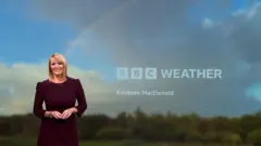 Woman wearing burgandy dress, with blue sky and rainbow in the background.