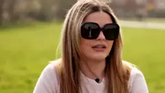 Annabelle Mackay sitting outside in a white t-shirt and dark sunglasses 