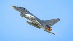 British Royal Air Force Eurofighter Typhoon jet flies upwards into a clear blue sky.