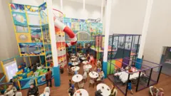A picture of the proposed soft play at the Life Centre. It is a large space with toys and the soft play itself. There is also tables and chairs to the front of the image.