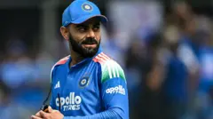 Virat Kohli looks behind, while polishing his sun glasses. He is wearing an India shirt and cap