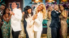 The King's message tops Christmas Day TV ratings 4 Claudia Winkleman and Tess Daly, both wearing white, join hands as they dance towards the camera, with judges and professional dancers behind them