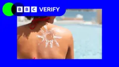 a view of a woman's shoulder from behind with sun cream lotion in the shape of a sun on her skin. she is next to a pool on a very sunny day