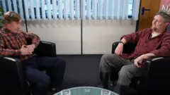 Alan Partridge sitting down opposite his old sidekick, Simon