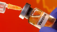 A small bottle labeled with a "Vaccine" sticker is held near a medical syringe
