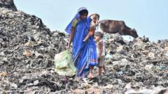 A woman carries her child as she collects firewood at a waste site in India