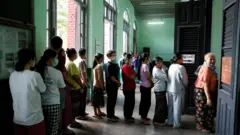 EPA/Shutterstock A line of people, many of them wearing face masks, wait to vote.