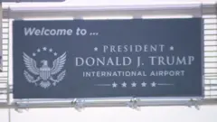 Image shows a sign saying "Welcome to President Donald J Trump International Airport"