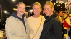 Nel family Three women looking at the camera and smiling. The pic is taken outdoors at night.