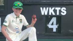 Owen Forbes holding the match ball in front of the scoreboard