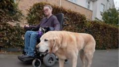 دبی شوارتز روی صندلی اتوماتیک مخصوص حمل این نوع بیماران، همراه با سگش در خیابان