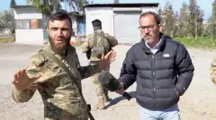 Syrian Soldier Ministry Defense Mahmud al-hoi gatherates as BBC NEWS Arabic Feros Khotoni has a microphone to al-Khaika