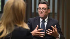 Burnham gestures as he speaks to the BBC's Laura Kuenssberg, who sits with the back of her head to camera.