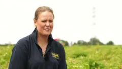 Polly Megginson pictured in a farmer's field. She has fair-coloured hair and is wearing a blue polo shirt.