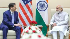 Marco Rubio (left) and Narendra Modi (right) smile at each other as they sit beside their respective countries' flags.