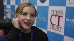 Sofia, who has blonde hair and is wearing a black jumper, can be seen smiling at the Isle of Wight Chess Tournament at Ryde School.