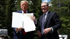 Reuters US President Donald Trump holds a printed copy of the UK-US tariff deal at the G7 summit in Canada. He stands next to British Prime Minister Sir Keir Starmer who is smiling