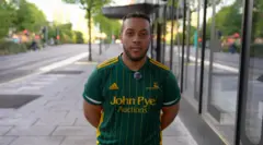 Jack Hudson, 21, electrician from Nottingham, stands in a busy street with his arms behind his back, wearing a cricket T-shirt
