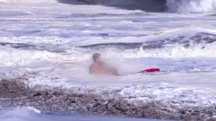 A life guard holds a child in the ocean.