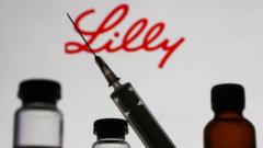 Fotografia colorida mostra uma seringa com agulha em primeiro plano e alguns frascos no fundo; o logotipo da Lilly está escrito na parede