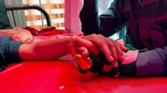 Person holds hand of victim on hospital bed
