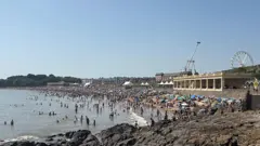Barry Island beach is packed with beach-goers and you can see the Barry Island pleasure park in the background. 