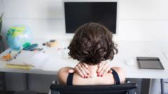 컴퓨터가 놓인 책상 앞에서 목을 감싸고 있는 여자의 뒷모습