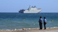 Papua New Guinea police officers on the foreshore watch an Australian warship off the coast