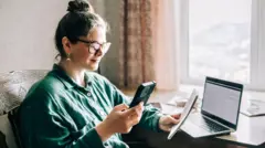 Woman looks at mobile and pad while working on a computer at home.