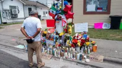 A man observes a makeshift memorial for Lorenzo Salgado Araujo, which features candles, ballons, and the Mexican flag.