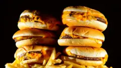 PA Media A stack of six cheeseburgers is placed on top of a portion of chips in front of a black background.