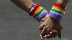 Two people holding hands wearing rainbow wristbands