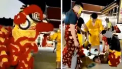 Men dressed in red and yellow lion dancing outfits hold a man to the ground with his arms behind his back.