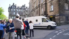 PA Media A white van outside a stone building, with photographers crowding around it 