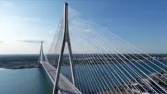 An aerial view of a long bridge connecting the US and Canada, with blue skies and water.