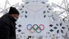 A man wearing a mask and coat walks past a building bearing the Olympics logo