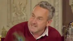 Hugo speaking at the breakfast table with an angry look