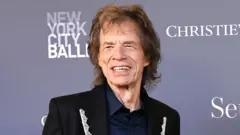 Mid-shot of Sir Mick Jagger, wearing a lace lapelled suit jacket