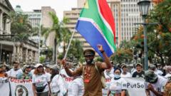 A member of Operation Dudula waves the South African national flag as others sings and chant anti-migrant slogans during their KwaZulu Natal operations launch at Durban City Hall in Durban on April 10, 2022