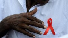 A Sri Lankan prisoner gestures towards a red ribbon on his chest as he takes part in a gathering to mark World AIDS Day at a prison complex in Colombo on December 5, 2015. AFP PHOTO / LAKRUWAN WANNIARACHCHI / AFP / LAKRUWAN WANNIARACHCHI