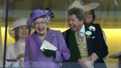 A rainha Elizabeth 2ª e John Warren com sorrisos abertos e em pé em camarote