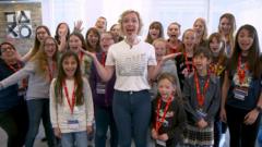 A group of young girl gamers stand behind alex as they shout with joy
