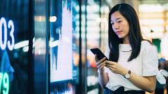 Woman looking at phone in front stock market graphics.
