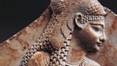 Fotogradia mostra estátua em pedra alaranjada de uma mulher com tranças e ornamentos no cabelo