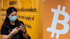 A woman wearing a mask stands next to a bus stop covered with Cryptocurrency electronic cash Bitcoin advertisement in Hong Kong.
