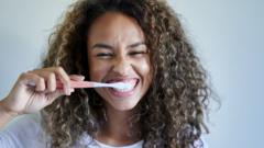 Cheerful young woman enjoying while brushing teeth against wall
