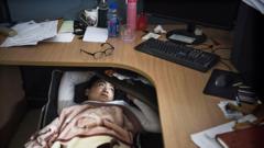 A tech worker taking a lunch break on a fold out bed under his desk