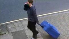 Jemma Mitchell pulling a blue suitcase through the streets of London